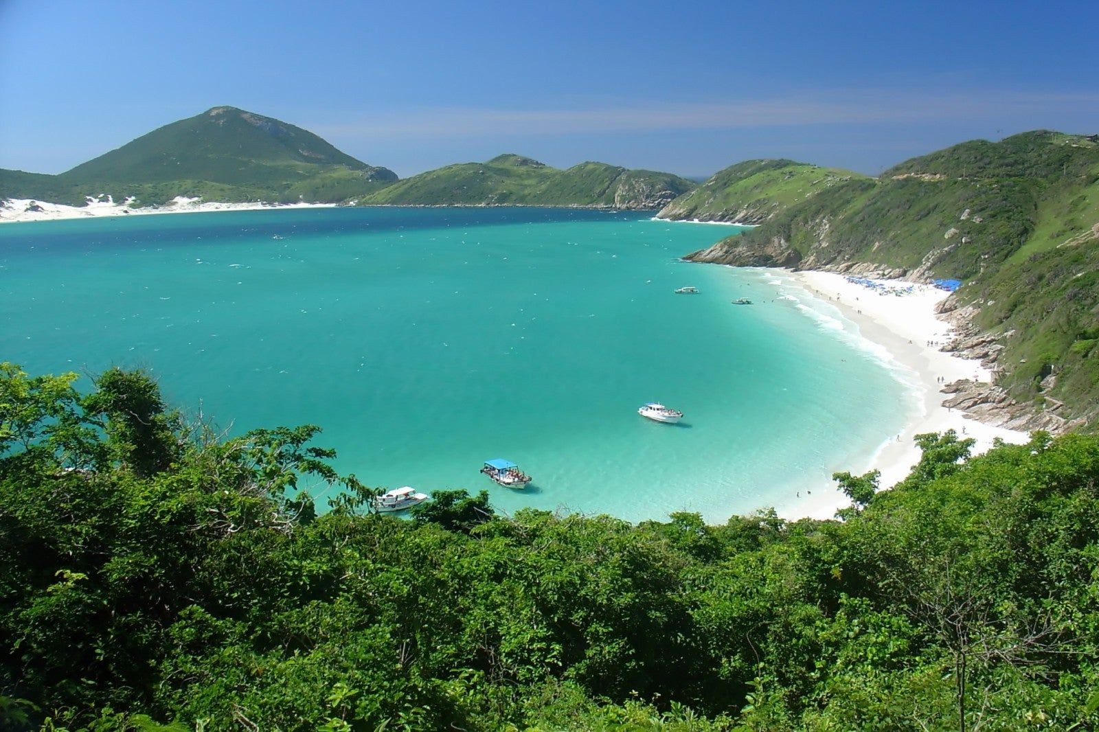 Bahía de Arraial do Cabo con aguas turquesas, montañas verdes y embarcaciones.